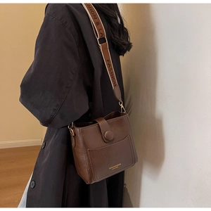 Détail du sac carré en cuir marron foncé avec large bandoulière en toile et texte doré