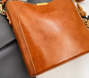 Close-up of caramel brown PU leather bucket bag with gold logo and soft pleated texture
