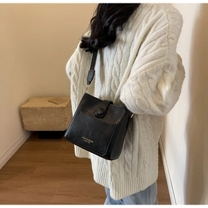 Détail du sac seau en cuir noir avec lettrage doré porté sur un pull en maille blanc