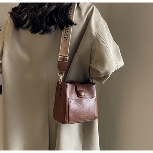 Gros plan d'un sac seau vintage en cuir marron avec une large bandoulière en toile brodée
