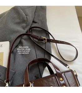Dettaglio della borsa a secchiello in pelle marrone scuro con tracolla regolabile e fibbie oro