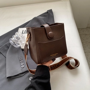 Détail du sac seau en cuir marron foncé avec lettrage doré et large bandoulière