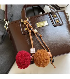 Dettaglio della borsa a secchiello in pelle cerata marrone scuro con charm a pompon