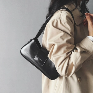 Side view of a chic black glossy PU leather shoulder bag worn with a beige trench coat
