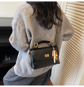 Détail du sac à main en cuir noir avec texture litchi, fermoir doré et perles