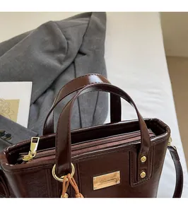 Dettaglio borsa a secchiello in pelle marrone con logo in metallo dorato e finiture