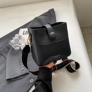 Détail du sac seau vintage en cuir noir avec lettrage doré et large bandoulière tissée
