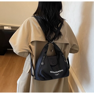 Detail of black nylon tote bag with white text logo worn over a beige trench coat