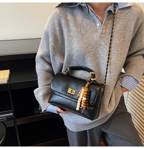 Détail du sac noir en cuir grainé avec fermoir doré tournant et breloque en perles de bois