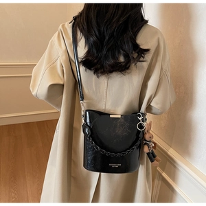 Detail of black glossy PU bucket bag with rabbit pendant and brand lettering on strap