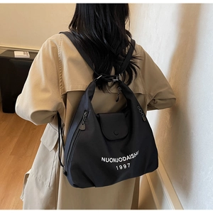 Detail of black nylon tote bag with side zipper pockets and white brand lettering