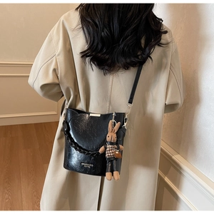 Detail of black textured PU leather bucket bag with cute rabbit pendant and brand lettering
