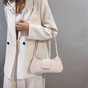Detail view of a minimalist cream PU leather baguette bag on a white blazer outfit