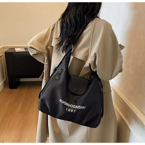 Detail view of large black nylon tote bag showing the side zipper and top leather buckle