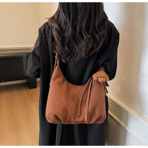 Model view of a brown suede hobo bag with a teddy charm in a minimalist interior