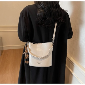 Detail of minimalist cream bucket bag featuring braided handle and cute rabbit charm accent