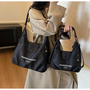 Detail of black canvas tote bag set with brand lettering and silver hardware accents