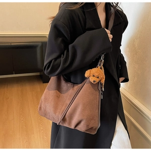 Brown suede hobo shoulder bag with a cute plush dog charm worn by a model in a suit