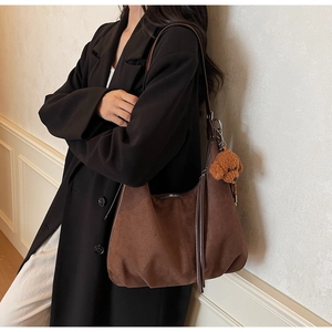 Brown suede crescent tote bag with fringe details and a teddy bear pendant on model