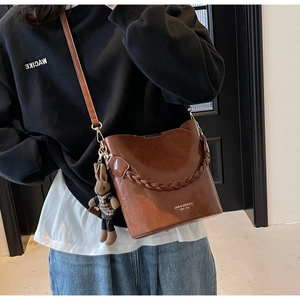 Detailed view of brown PU leather bucket bag with woven handle and plush bunny charm