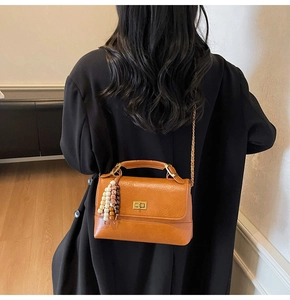 Détail du sac bandoulière en cuir caramel avec fermoir doré et breloque perlée sur modèle