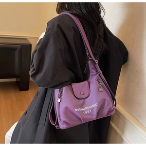 Detail view of purple nylon tote bag showing multiple zipper pockets and brand lettering