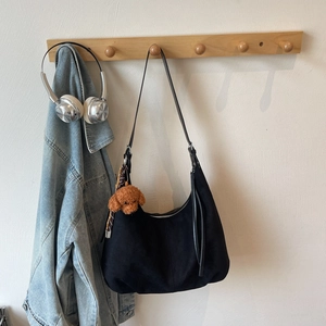Detail of black hobo bag in matte suede leather with cute brown teddy bear keychain pendant