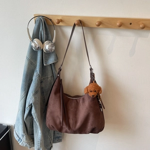 Detail of dark brown hobo bag featuring a plush teddy bear charm and top zipper