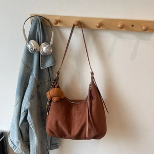Detail of a brown suede hobo bag with long tassels and a cute plush bear charm on a rack