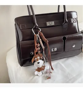 Detail einer glänzenden schokobraunen Tragetasche mit Vordertaschen und süßem Hundeanhänger