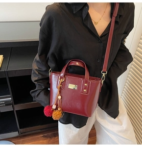 Dettaglio borsa a secchiello bordeaux in pelle PU con logo dorato e ciondolo a pompon