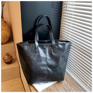 Detail einer schwarzen Leder-Tote-Bag mit vertikaler Naht auf einer Holzoberfläche