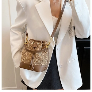 Detail of a brown woven tweed bucket bag with leather trim worn by a model in a suit