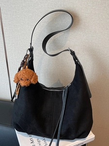 Retro black suede tote bag with brown plush puppy charm on a white book surface
