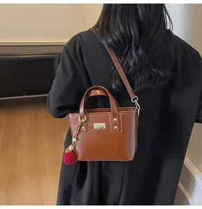 Mini borsa a secchiello marrone in ecopelle con placca logo e ciondolo pompon colorato