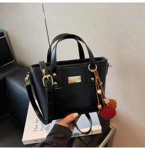 Dettaglio della borsa a secchiello in PU nero opaco con finiture oro e charm a pompon