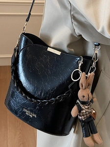 Minimalist black PU bucket bag with pleated texture and woven strap featuring a bunny charm