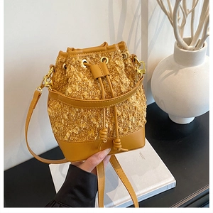 Detail of a bright yellow tweed drawstring bucket bag with leather trim and gold hardware