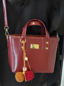 Elegante borsa a secchiello bordeaux lucida con ciondolo in peluche e dettagli oro