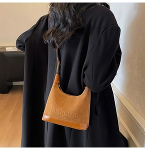 Sac sous l'aisselle en daim marron avec logo porté par un mannequin en manteau noir