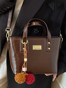 Secchiello marrone scuro lucido con dettagli dorati e ciondolo su abito nero