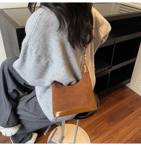Détails de sac hobo en daim marron avec lettrage embossé et boucles métalliques dorées