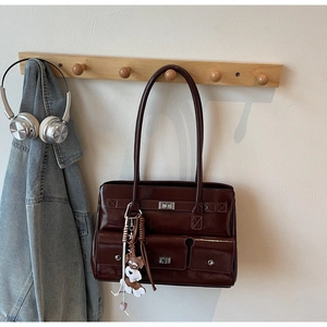 Detail der dunkelbraunen glänzenden Shopper-Tasche mit Metallschnalle und Plüsch-Anhänger