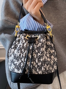 Fashionable tweed and leather bucket bag with gold hardware held by model in hand