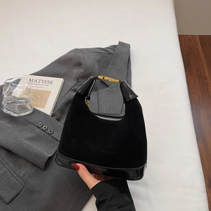 Détail du sac noir en daim et cuir verni avec boucle dorée tenu devant un costume gris