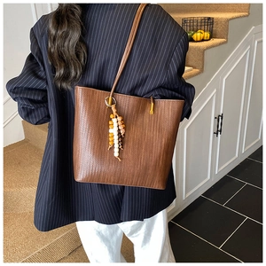 Détail d'un sac cabas marron à texture tressée avec un charme perlé sur la bandoulière