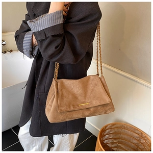 Sac fourre-tout en daim marron avec bandoulière chaîne dorée porté par un mannequin