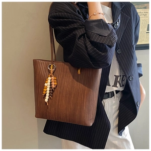 Gros plan sur un sac cabas marron avec texture tissée et pompon rétro en perles de bois