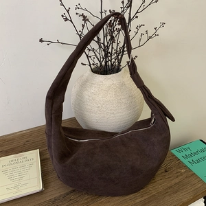 Detail of a dark brown suede hobo bag with silver zipper on a rustic wooden table