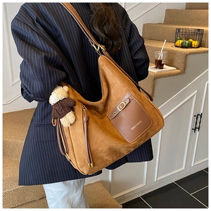 Close-up of brown suede shoulder bag with bear pendant and ZSKE PARIS leather pocket detail